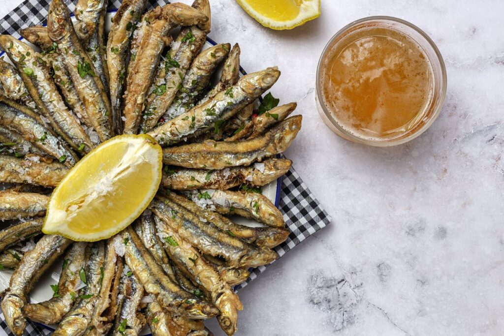 Anchiovies arranged circularly on a plate with a large slice of lemon in the center.