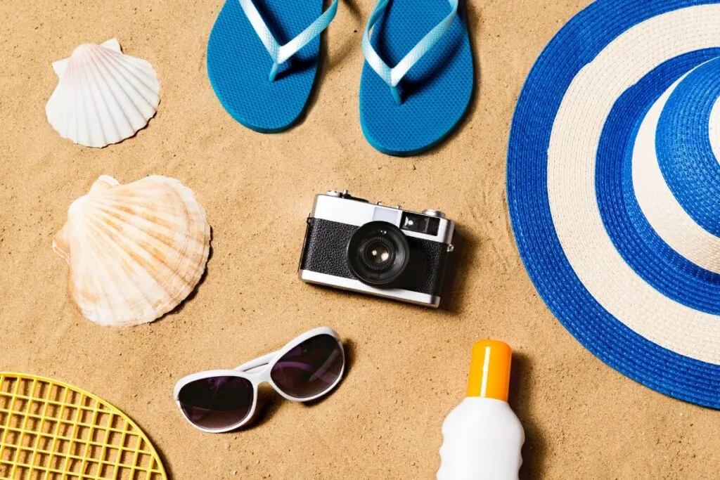 Blue flipflops, a blue and white wide brimmed hat, sun glasses, sunscreen and shells all of which should be things you pack for Hawaii. 