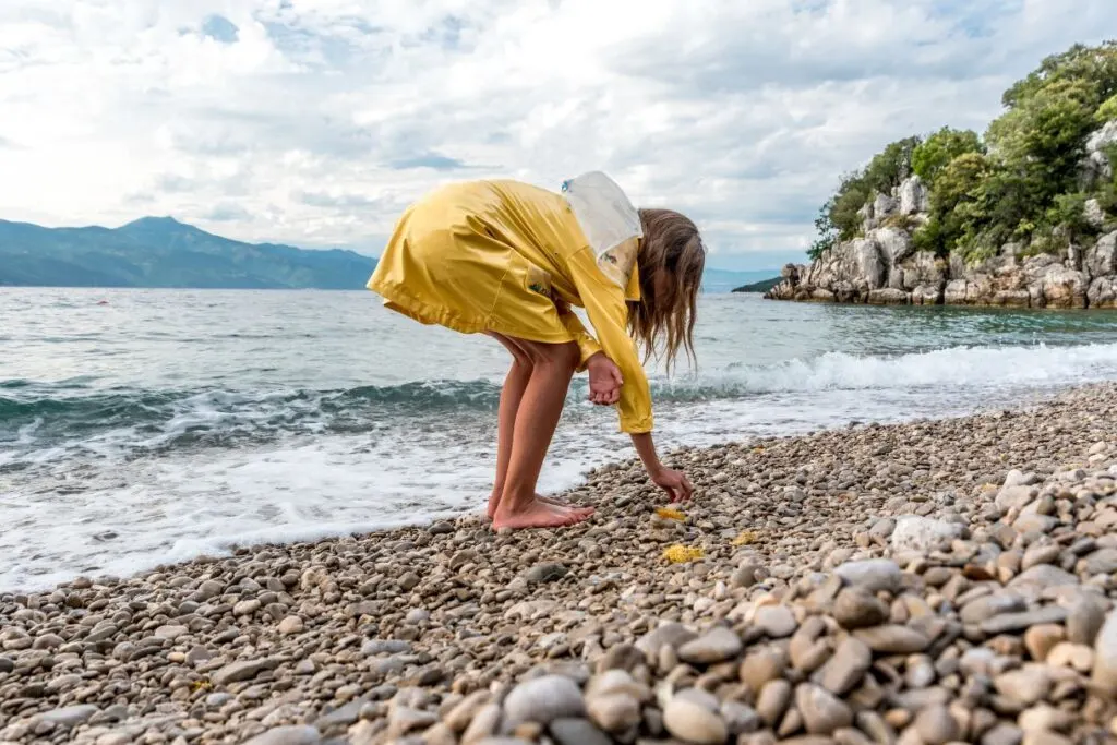 A girl in a yellow rain coat at the beach because a rain jacket is an essential when prepping your Hawaii packing list.