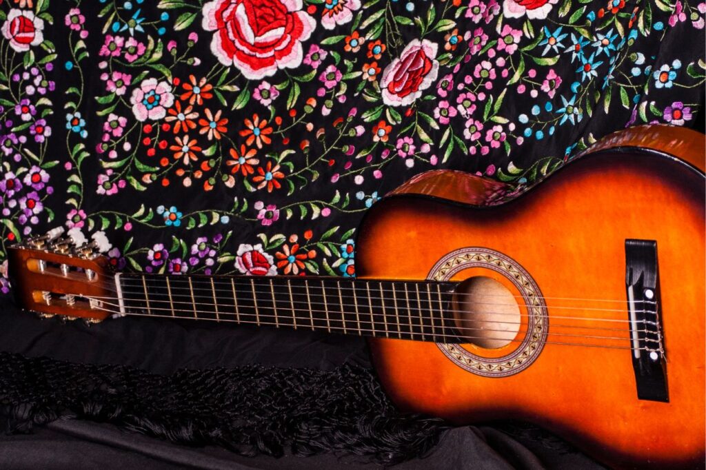 A brown guitar set against a black fabric with colorful flowers on it representing the famed flamenco which is one of the reasons why you should visit Malaga.