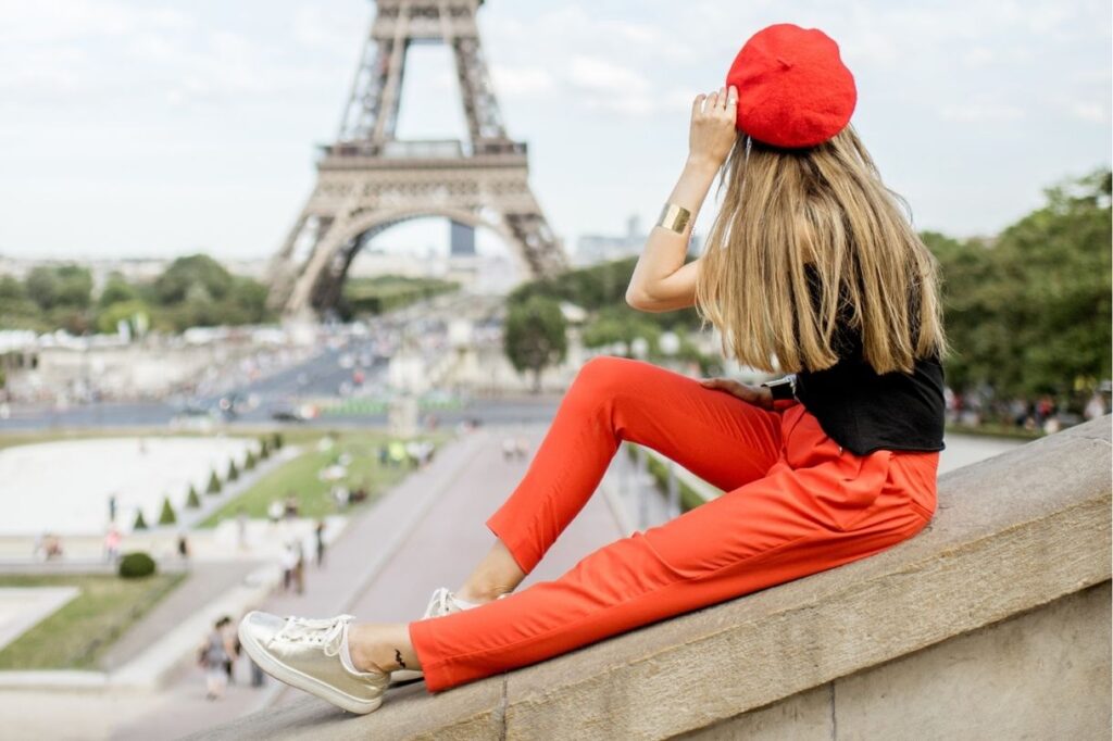 A lady sitting on the wall with the eiffel tower in the background and a red beret which is one of the best Paris gifts that you could get