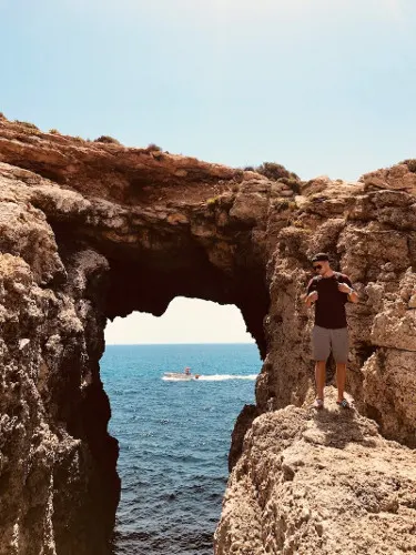 A arched path with a view of the sea and a man standing on a rock next to it is another iconic sight to see during your 3 days in Malta itineray.