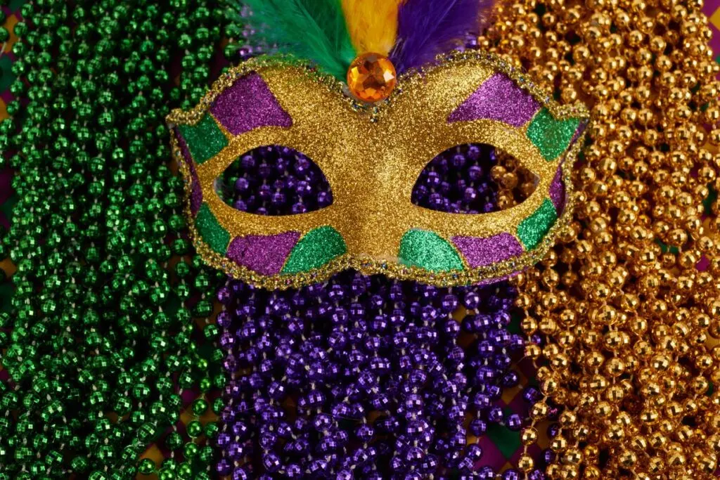 A golden mask with green and pink glitter and colorful beads behind it is just one of the many inspirations for these cool New Orleans quotes and captions on Mardi Gras