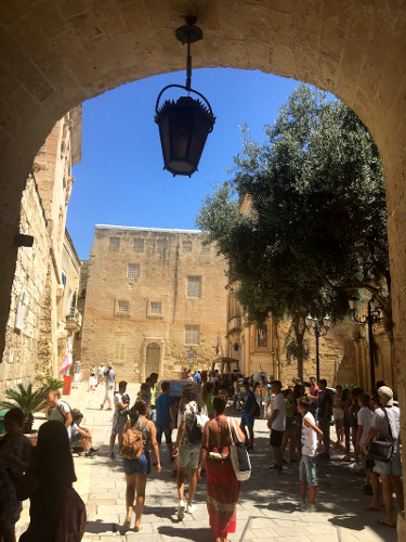 A beautiful arched entry with a lantern and lots of people walking through it in Mdina which is one of the cool places to visit during your 3 days in Malta itinerary.