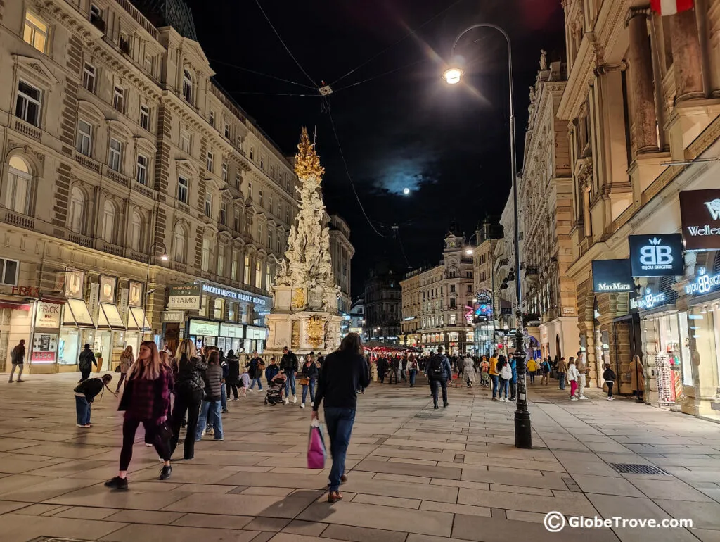 The column of Pest in the night with busy tourists and shoppers.